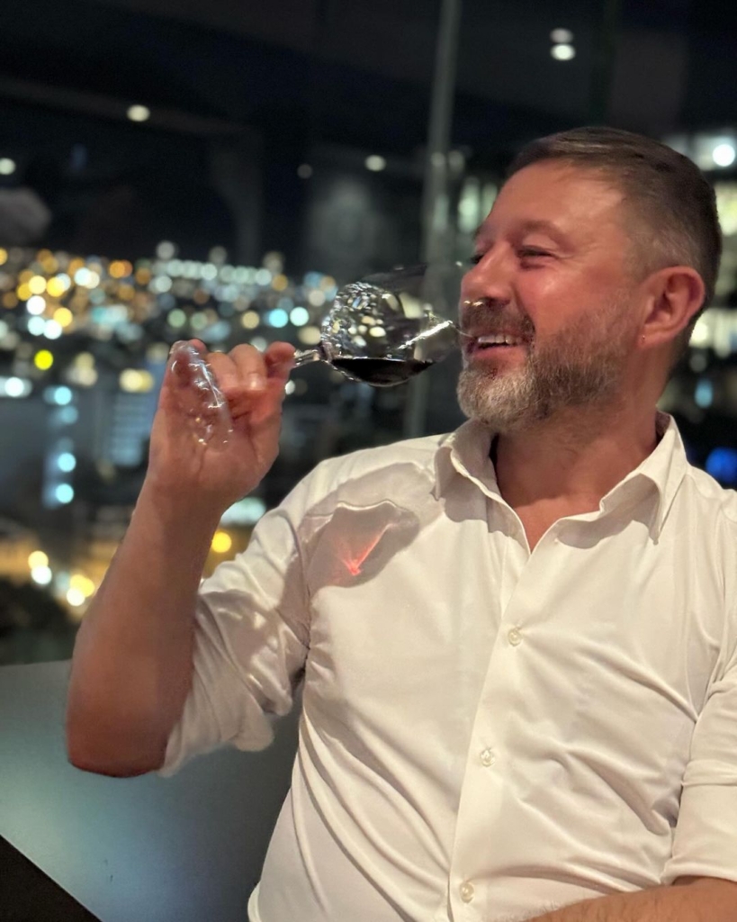Andrzej Piaseczny pije wino na tle nocnego miasta