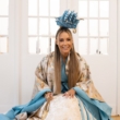 Małgorzata Rozenek-Majdan klęczy w biało-niebieskiej, barokowej sukni i ze statkiem na głowie.